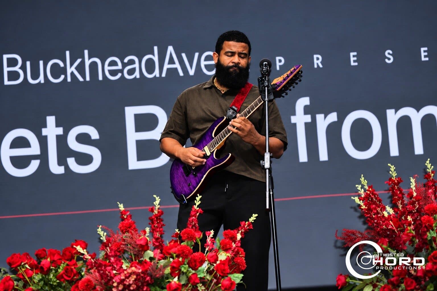 Guitarist performing on a stage lined with red flowers